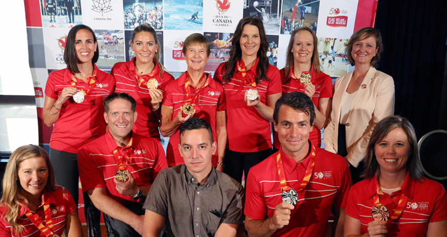 Group of people smiling and holding medals at a ceremony, wearing red and white uniforms.